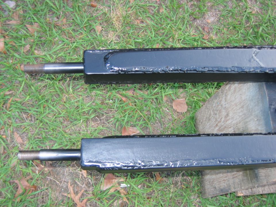 Two black metal trailer hitch receivers with threaded shafts on grass