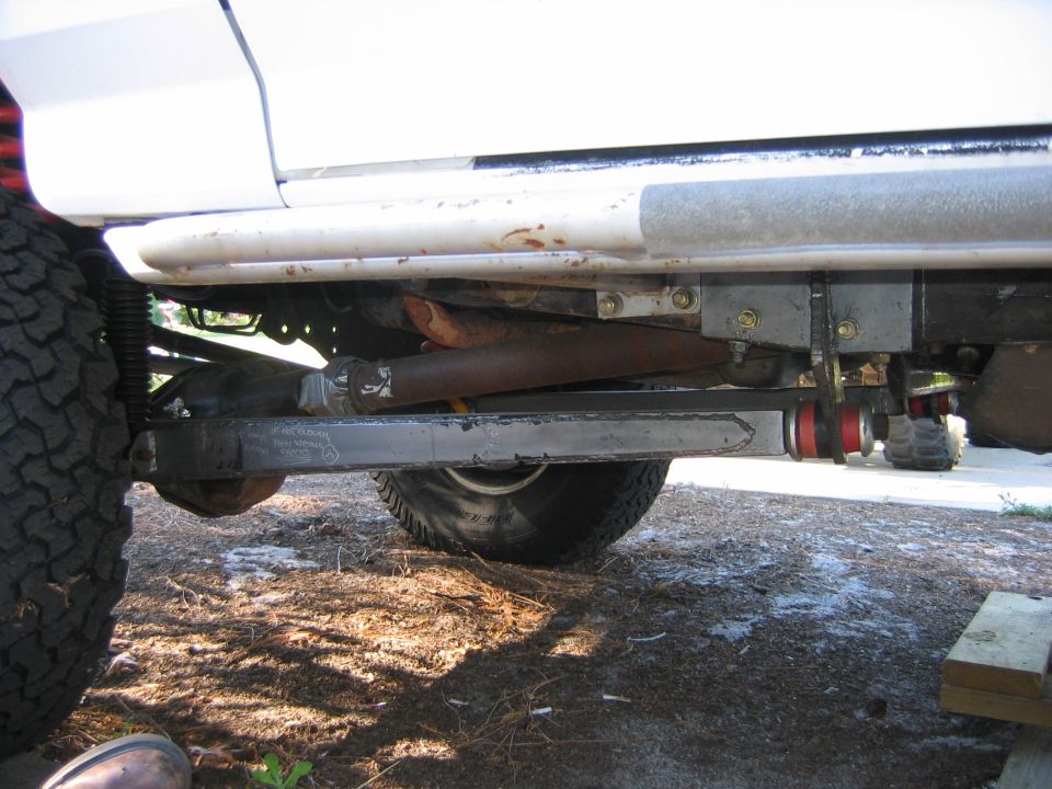 Underside view of a white vehicle's modified suspension with control arm and red bushings.