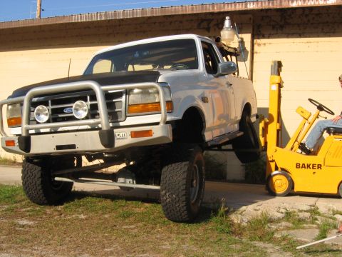 1992 Ford Bronco - A lifted 1992 Ford Bronco is parked next to a yellow vehicle under a clear sky.