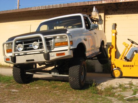 1992 Ford Bronco - A silver SUV with a brush guard and large tires is parked outdoors.