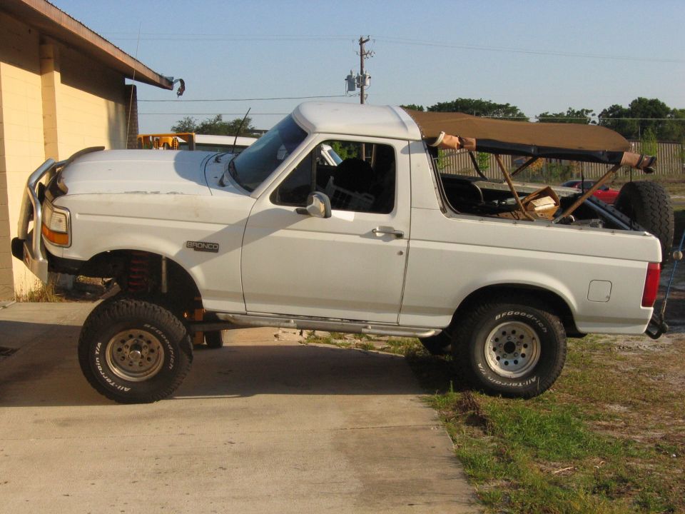 Lifted white 1992 Ford Bronco with tan soft top and brush guard.