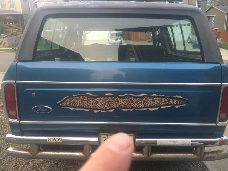 Rear view of a blue Ford Bronco with a camouflage decal and a "Wild Child" sticker on the bumper.