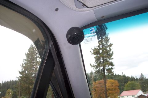 1995 Ford Bronco - A small, black speaker is mounted on the interior pillar of the vehicle, with a view of trees outside.