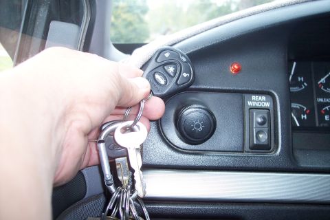 1995 Ford Bronco - A hand holds car keys and a remote control near the dashboard, which includes a button labeled 'REAR WINDOW'.