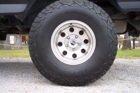 1995 Ford Bronco - A close-up view of a BFGoodrich All-Terrain tire mounted on a silver multi-hole rim.