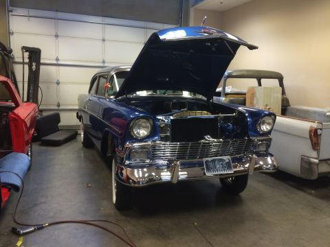 1964 Ford Fairlane - A blue 1956 Chevrolet sedan is parked in a garage with its hood open, alongside other vehicles.