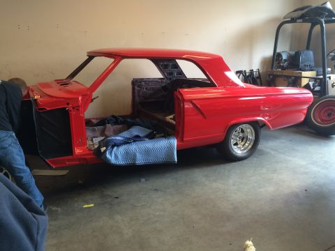 1964 Ford Fairlane - A person works on the body of a red classic car in a garage. The car is missing many parts.