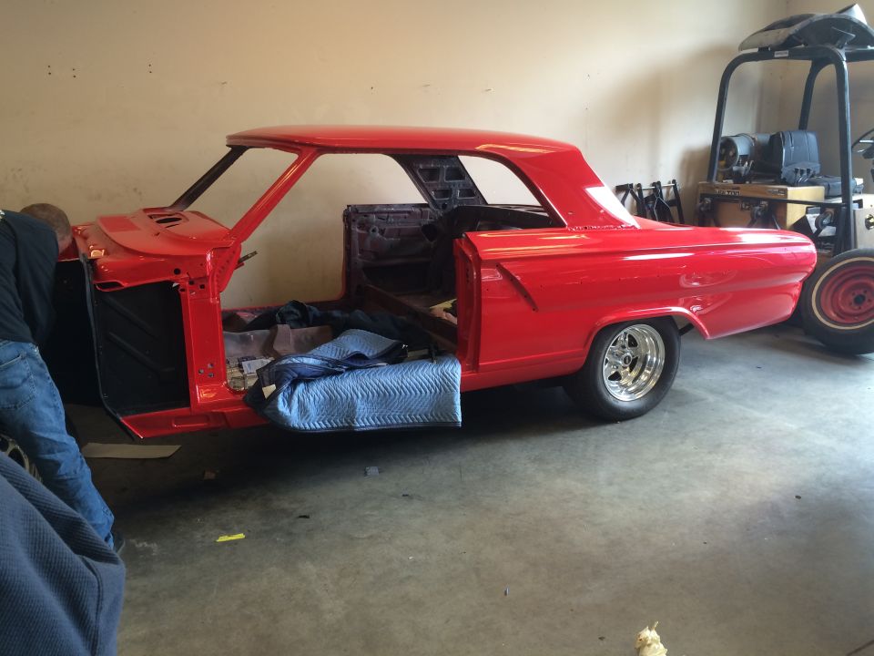 Red classic car body, doors open, being worked on. Blue padding on the floor inside
