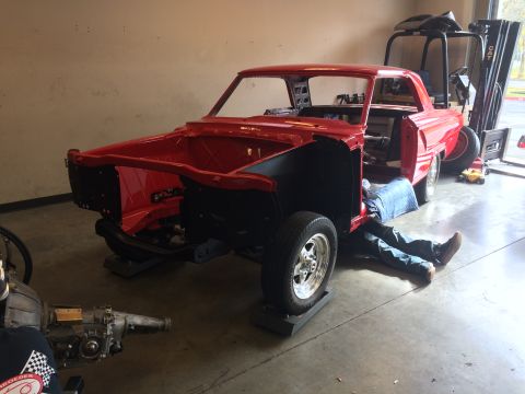 1964 Ford Fairlane - A red car body is being worked on in a garage, with a person lying underneath.