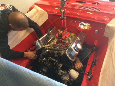 1964 Ford Fairlane - Engine being lowered into a vehicle's engine bay with assistance from a hoist and mechanics.