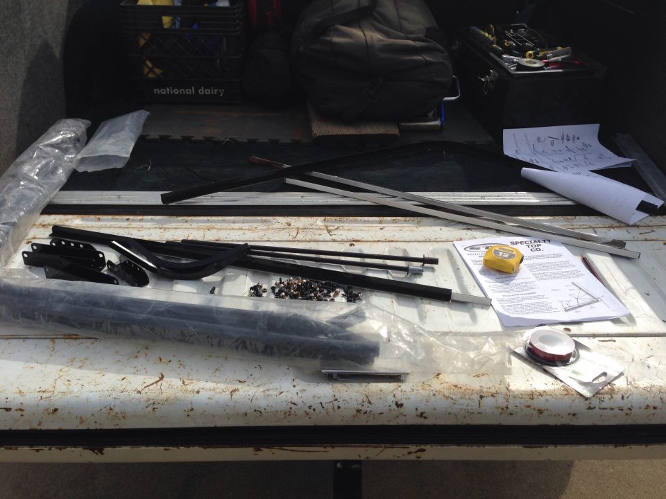 Parts and instructions laid out in the bed of a pickup truck. Includes metal bars, brackets, screws, and a tape measure