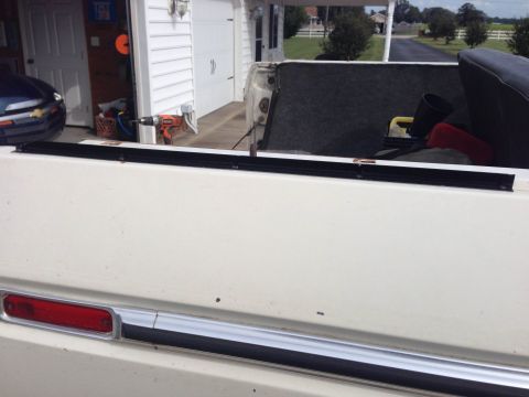 1979 Ford Bronco - Rear view of a white 1979 Ford Bronco, showing the tailgate with chrome accents and a red taillight.