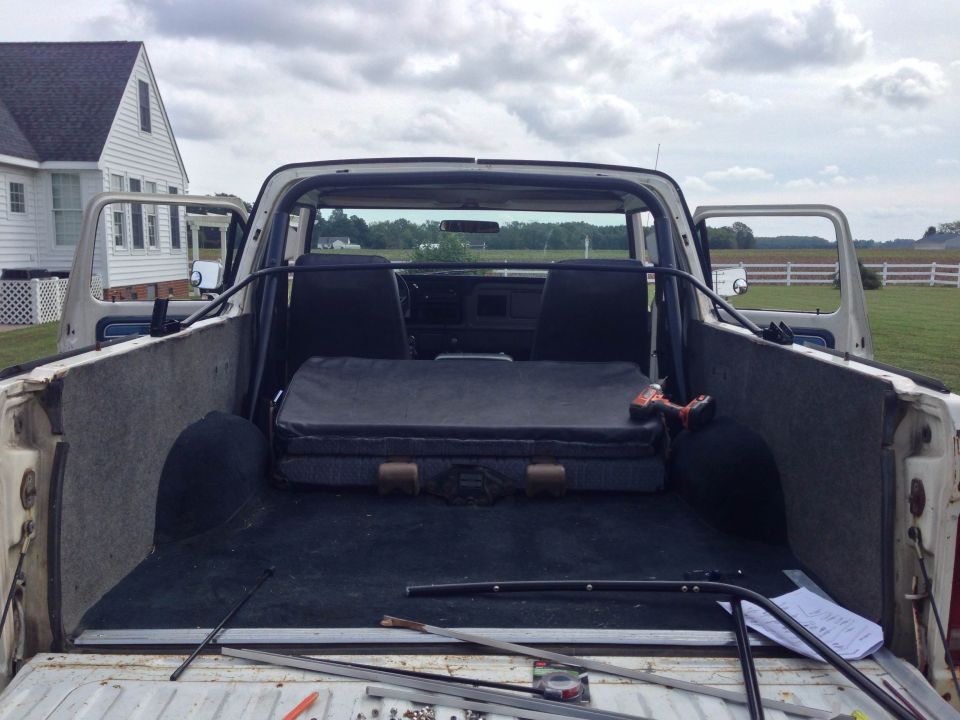 Rear interior view of a 1978 Ford Bronco with seats and cargo area visible. A toolbox and drill are in the cargo bed