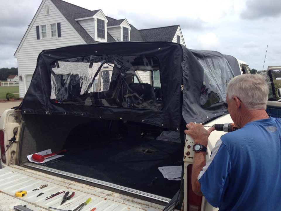Man drills into the side of a 1979 Ford Bronco while installing its soft top