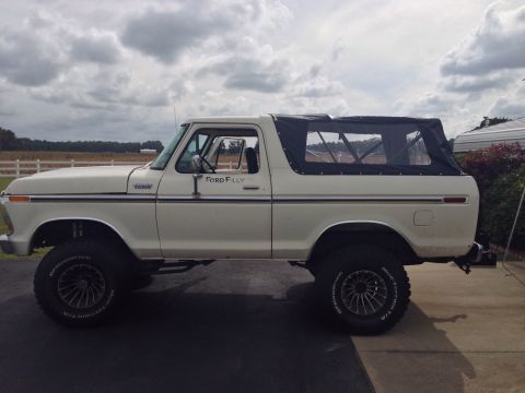 1979 Ford Bronco - Side view of a lifted Ford Bronco with a black soft top and custom wheels under a cloudy sky.