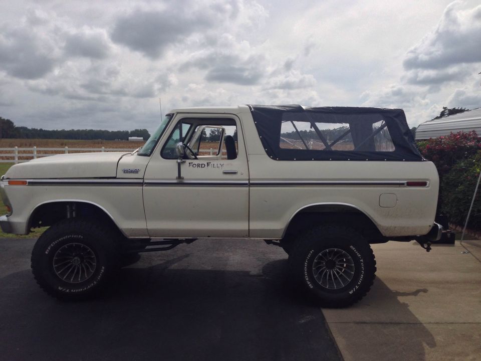 White Ford Bronco with black soft top, lifted on off-road tires. "Ford Filly" text on door