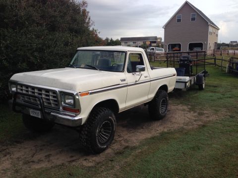 1979 Ford Bronco - A white 1979 Ford Bronco is parked on a dirt path, towing a trailer with a grill and cooler.