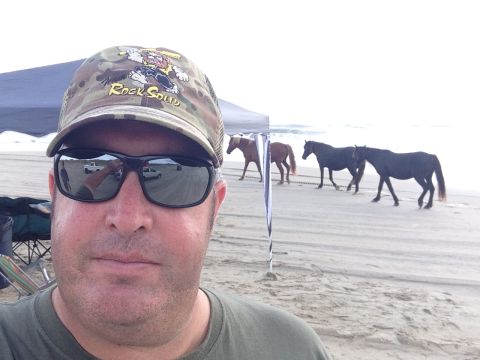 1979 Ford Bronco - A man takes a selfie on the beach as a group of horses walks past in the background.