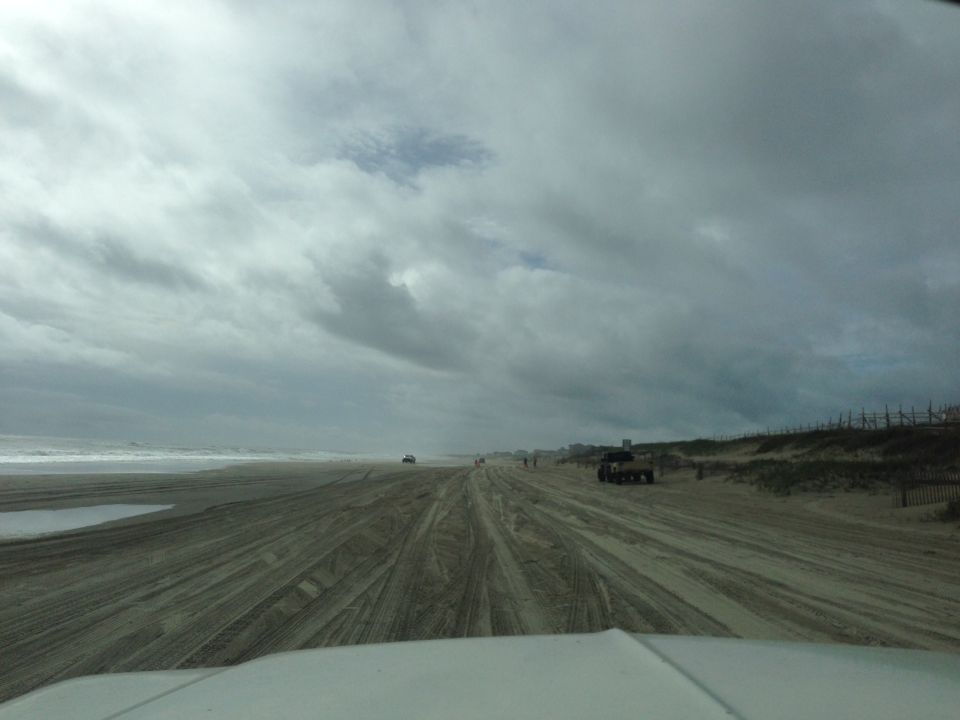 Several vehicles driving on a wide sandy beach under a cloudy sky