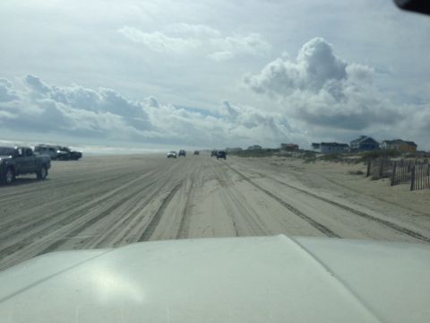 1979 Ford Bronco - A dark-colored pickup truck is parked on a sandy beach next to several other vehicles. The truck is viewed from the side at a 3/4 front ang…