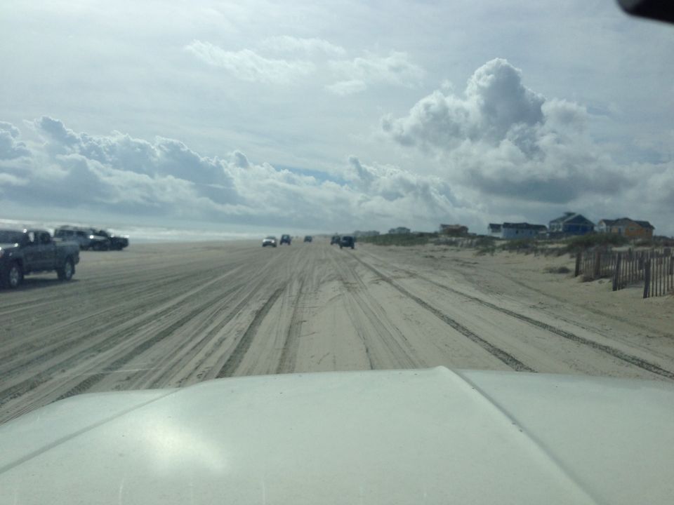 Dark pickup truck on a sandy beach with other vehicles.