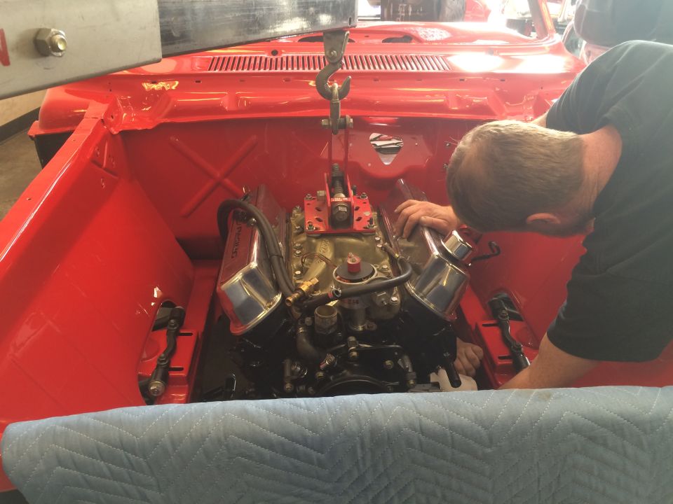Mechanic working on a red V8 engine with chrome valve covers in a vehicle.
