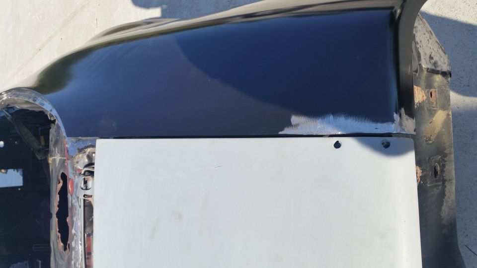 Close-up of a car's fender and door panel with black paint and gray primer.