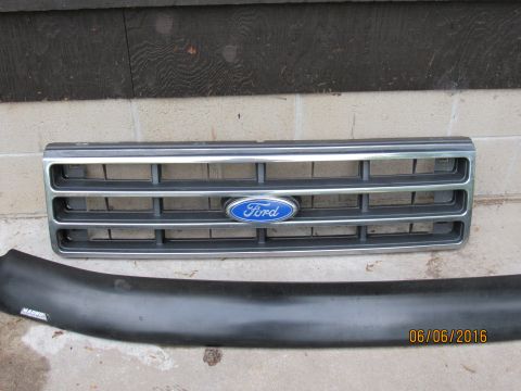 1978 Ford Bronco - A chrome and gray Ford truck grille with a blue Ford emblem is shown above a black plastic bumper or trim piece. The items are resting on a…