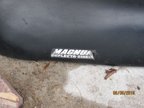 1978 Ford Bronco - A close-up view of a black Deflecta-Shield emblem on a vehicle part, possibly a fender or hood, resting on a concrete surface. The emblem r…
