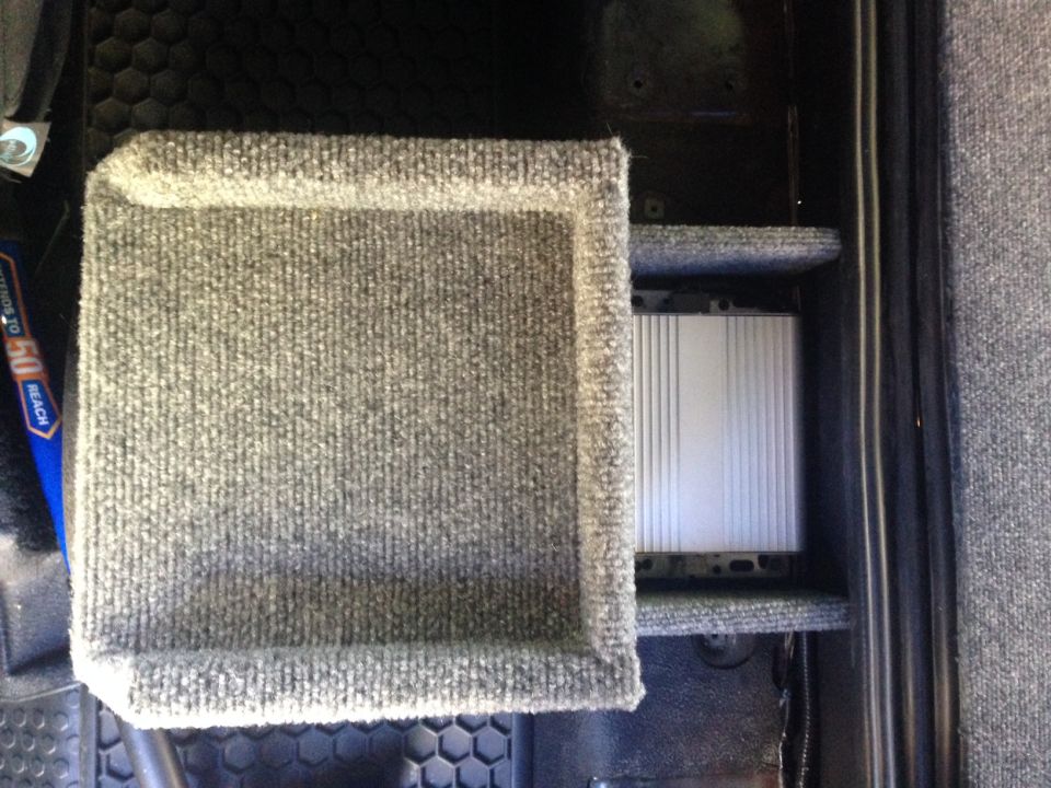 Carpeted compartment with silver amplifier underneath a shelf.