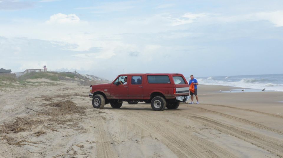 Red SUV parked on a beach with a man standing next to it.