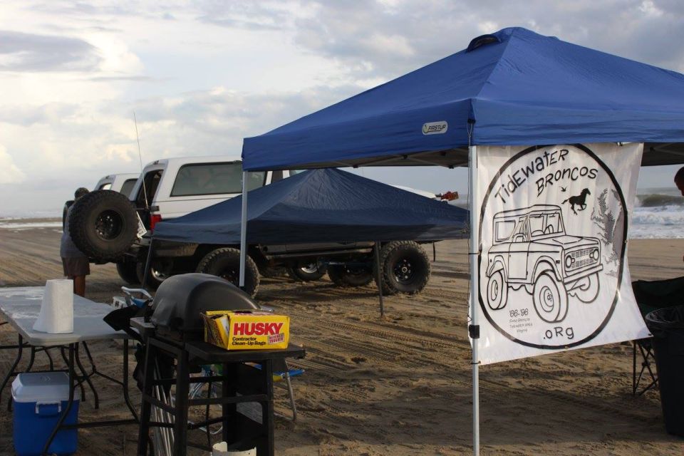 White Ford Bronco on a beach under a blue canopy with a custom banner.