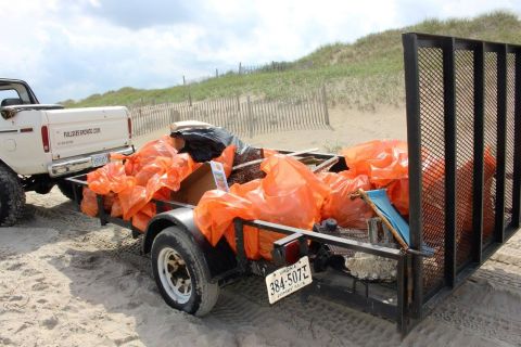 1979 Ford Bronco - A white Ford Bronco is parked on a sandy beach, towing a trailer filled with orange trash bags and debris. The trailer is attached to the r…