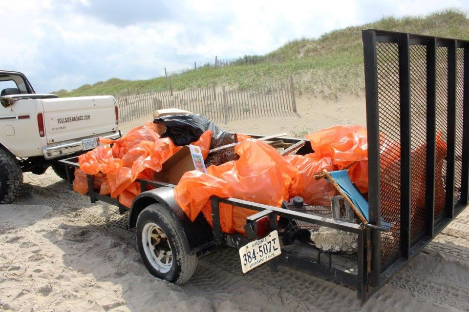 White Ford Bronco towing a trailer full of trash bags on a sandy beach.