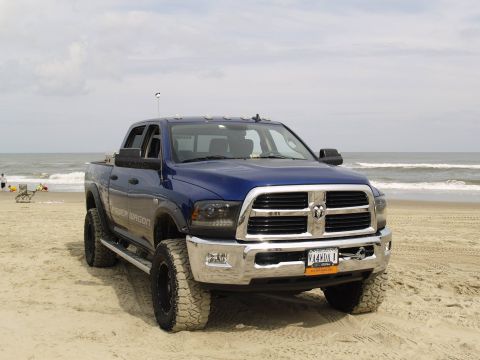 1979 Ford Bronco - A blue Ram Power Wagon pickup truck is parked on a sandy beach with the ocean in the background. The truck has large off-road tires and a c…