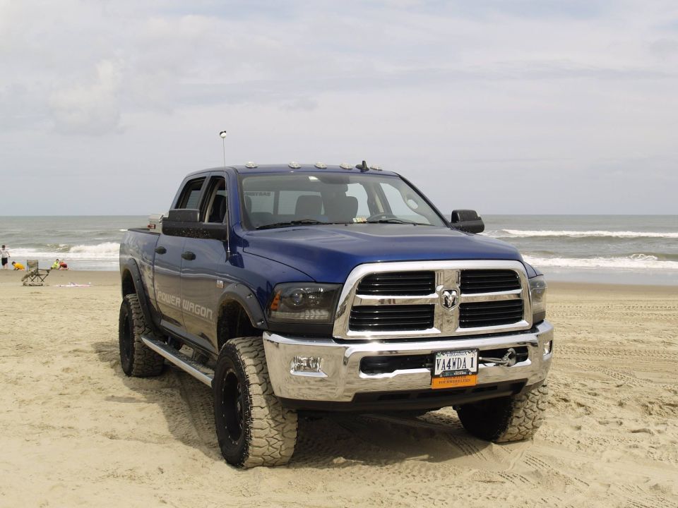 Blue Ram Power Wagon pickup truck on a beach with the ocean behind it.