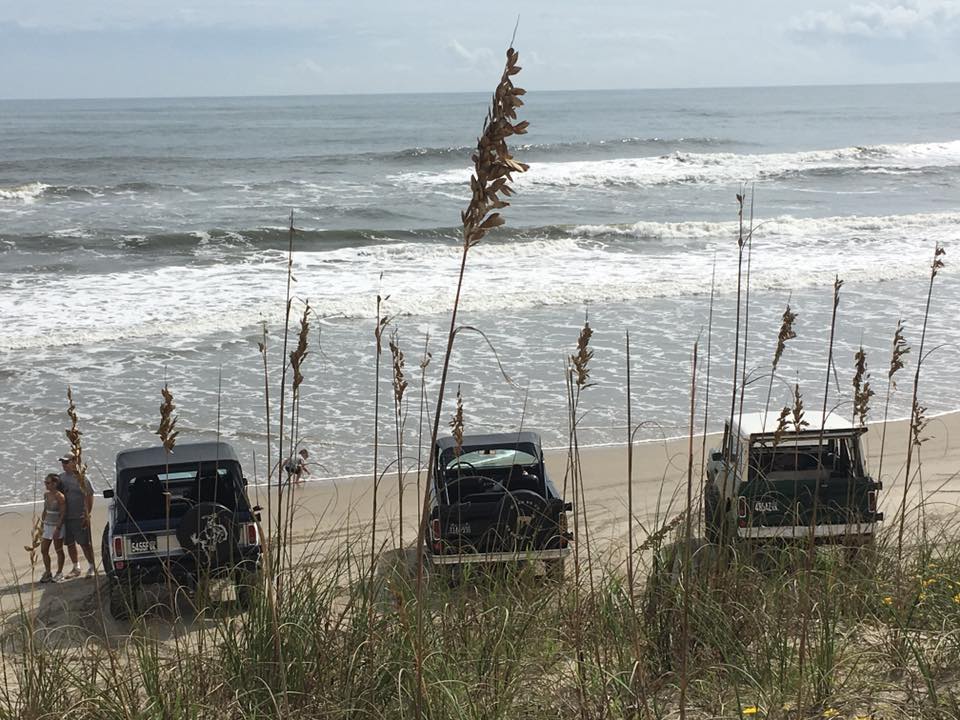 Three off-road vehicles on a beach with the ocean in the background.