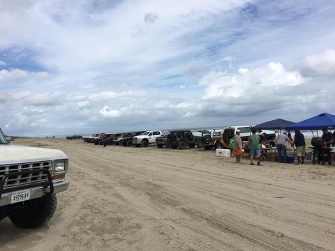 1979 Ford Bronco - A row of off-road vehicles are parked on a sandy beach under a cloudy sky. The front of a white 1979 Ford Bronco is visible in the foregrou…