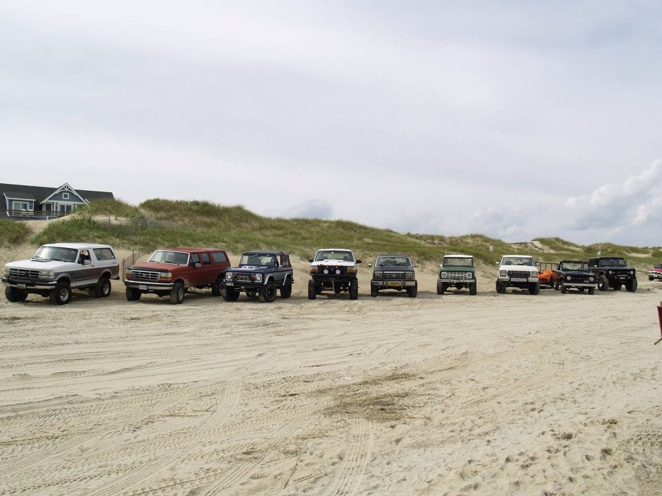 Multiple SUVs and trucks parked on a sandy beach.