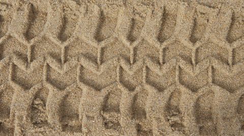 1979 Ford Bronco - A close-up overhead view of tire tracks imprinted in the sand.