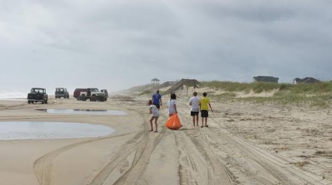 1979 Ford Bronco - Several off-road vehicles are parked on a sandy beach under a cloudy sky. A group of people are walking away from the vehicles towards sand…