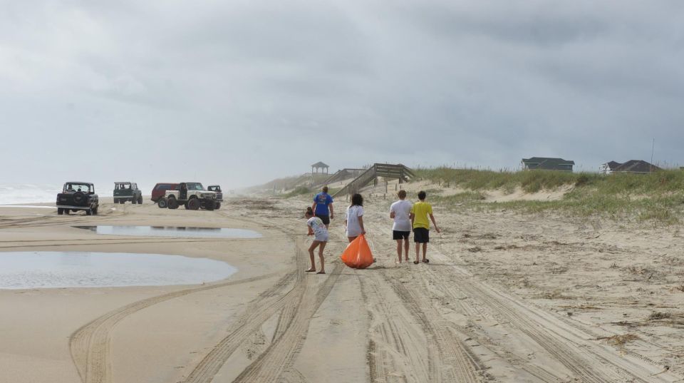 Off-road vehicles on a sandy beach with people walking towards dunes.