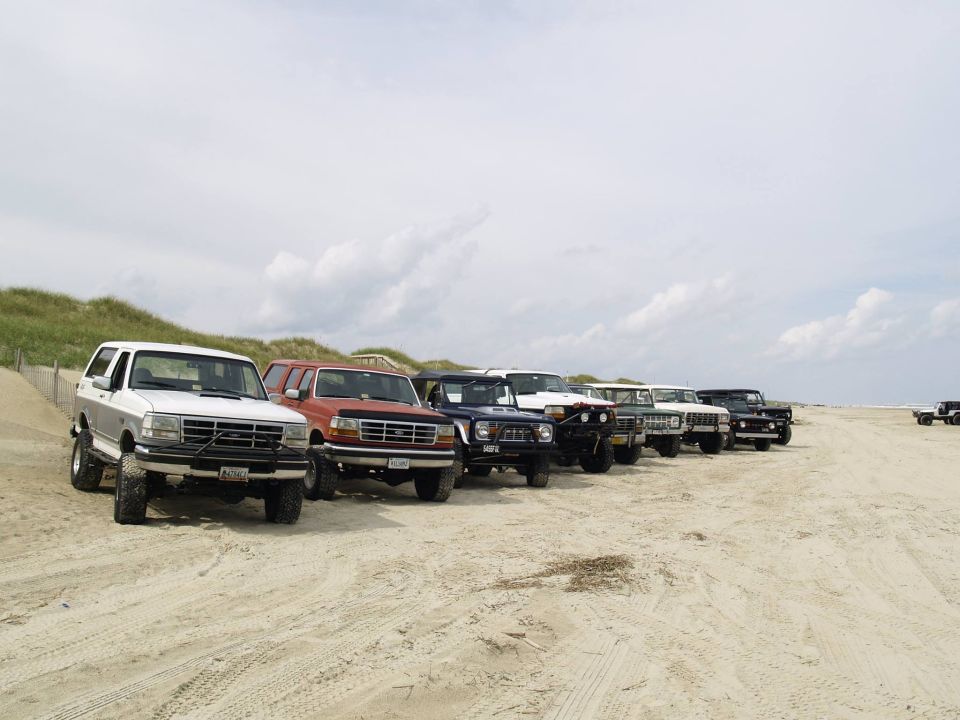 A line of SUVs and trucks parked on a sandy beach.