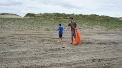 1979 Ford Bronco - Two people are on a sandy beach with sand dunes in the background. One person is holding an orange trash bag.