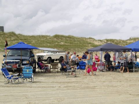 1979 Ford Bronco - A group of people are gathered on a sandy beach around a white 1979 Ford Bronco and a dark blue SUV. Two tents are set up, providing shade…
