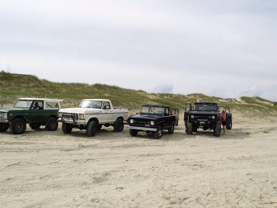 Four off-road vehicles parked on a sandy beach.
