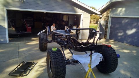 1985 Jeep CJ7 - A custom off-road vehicle frame with large tires is parked in a driveway in front of a garage. A person is seated inside the frame, working…