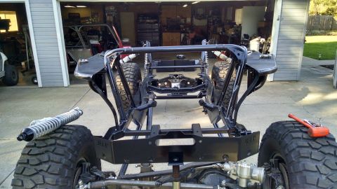 1985 Jeep CJ7 - The bare frame of a custom off-road vehicle, possibly a Jeep CJ7, is shown in a garage setting. Large, aggressive tires and suspension comp…