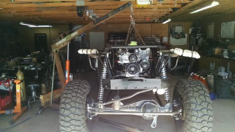 1985 Jeep CJ7 - A custom Jeep CJ7 is shown in a garage with its engine being lowered into place by an engine hoist. The vehicle has a roll cage and large o…