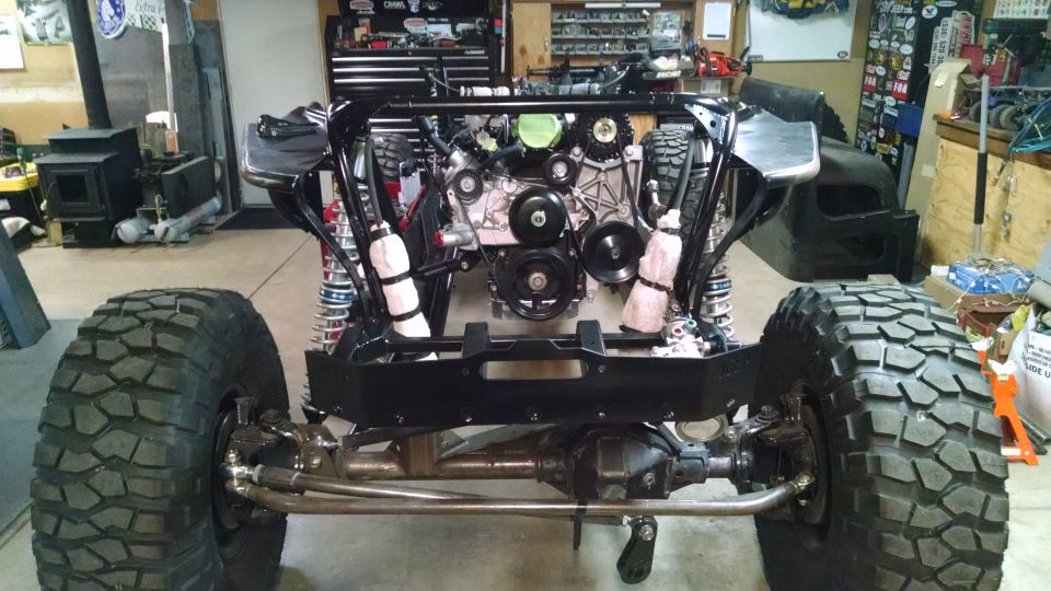 Custom off-road vehicle chassis with engine, suspension, and large tires in a garage.